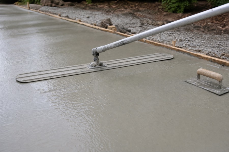 A magnesium bull float resting on freshly poured wet concrete inside wooden forms on a residential driveway