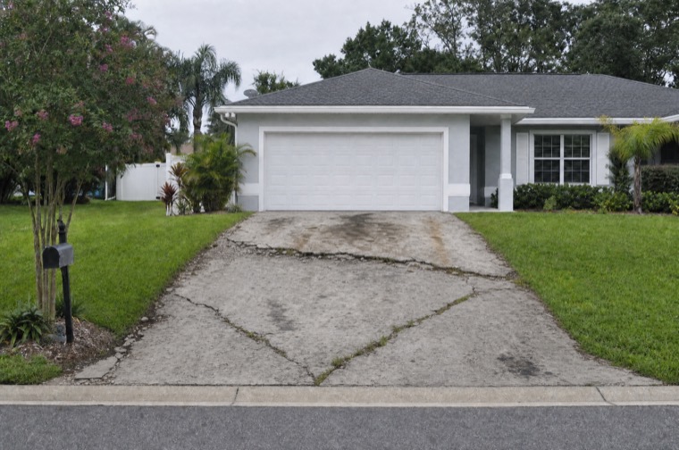A Central Florida driveway with wide cracks and a settled, broken section near the garage