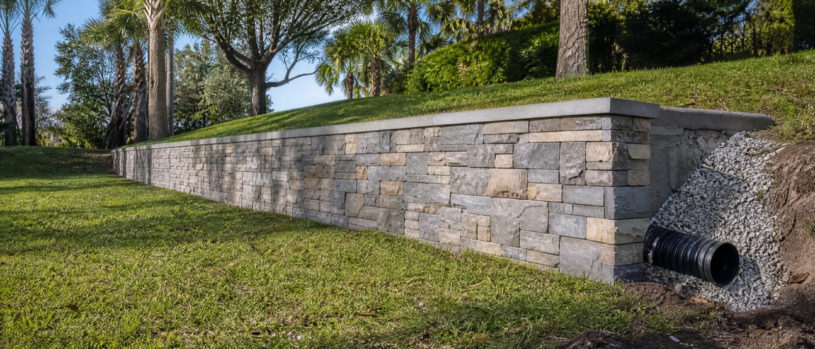 A new concrete block retaining wall with a stone veneer face holding a sloped Clermont yard, drainage gravel visible behind it