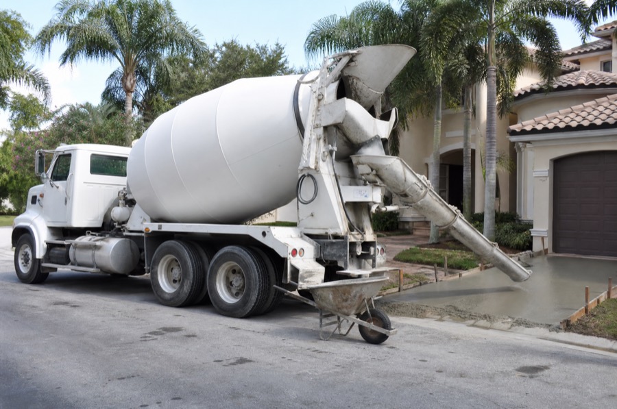 A plain unmarked concrete mixer truck at the curb of a Florida street with its chute extended toward a freshly formed driveway